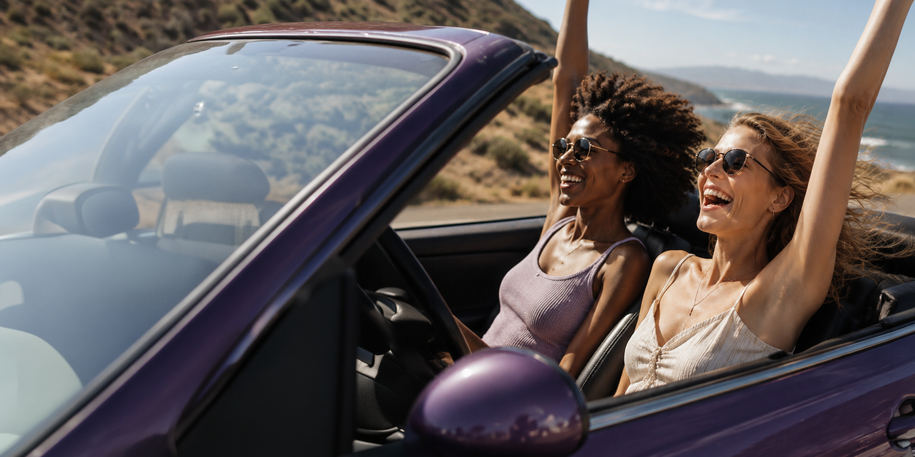 Two women laughing in a convertible car on a coastal road