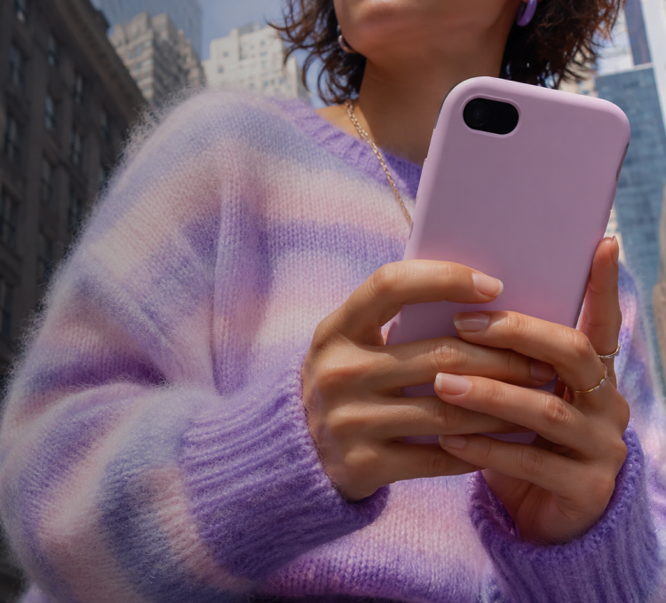 Person in a pastel striped jumper using a pink phone on a city street