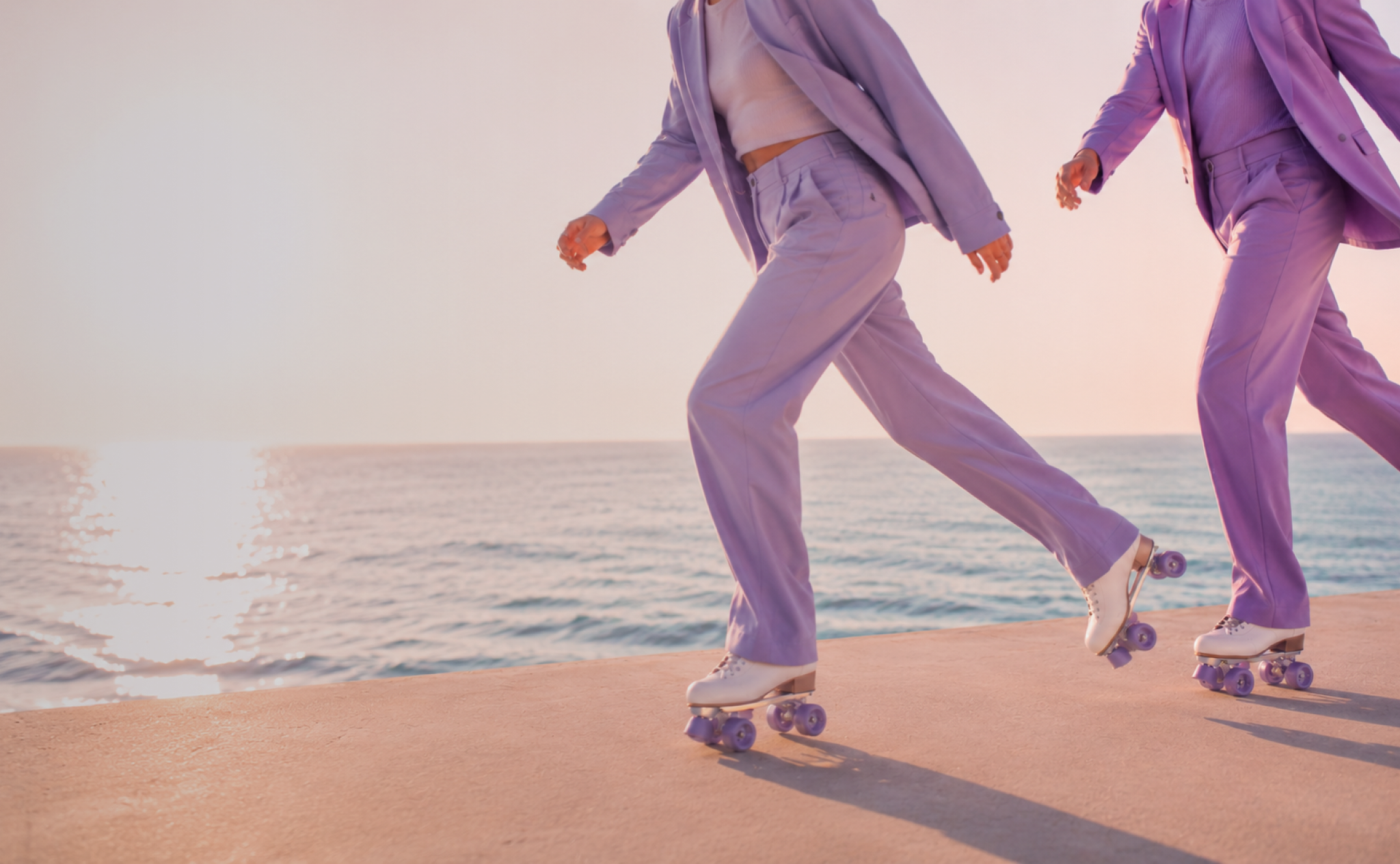 Two people rollerskating along a seafront in matching purple suits